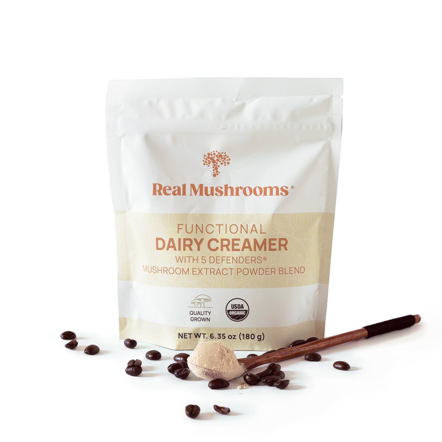 A bag of Real Mushrooms Functional Dairy Creamer Powder with a wooden spoon and coffee beans scattered around it on a white background.