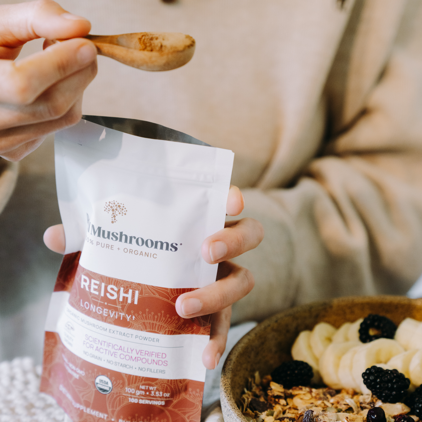 Someone scoops Real Mushrooms’ Organic Reishi Mushroom Powder – Bulk Extract with a wooden spoon over granola, banana, and blackberries—enjoying reishi’s natural beta-glucans and wellness benefits.