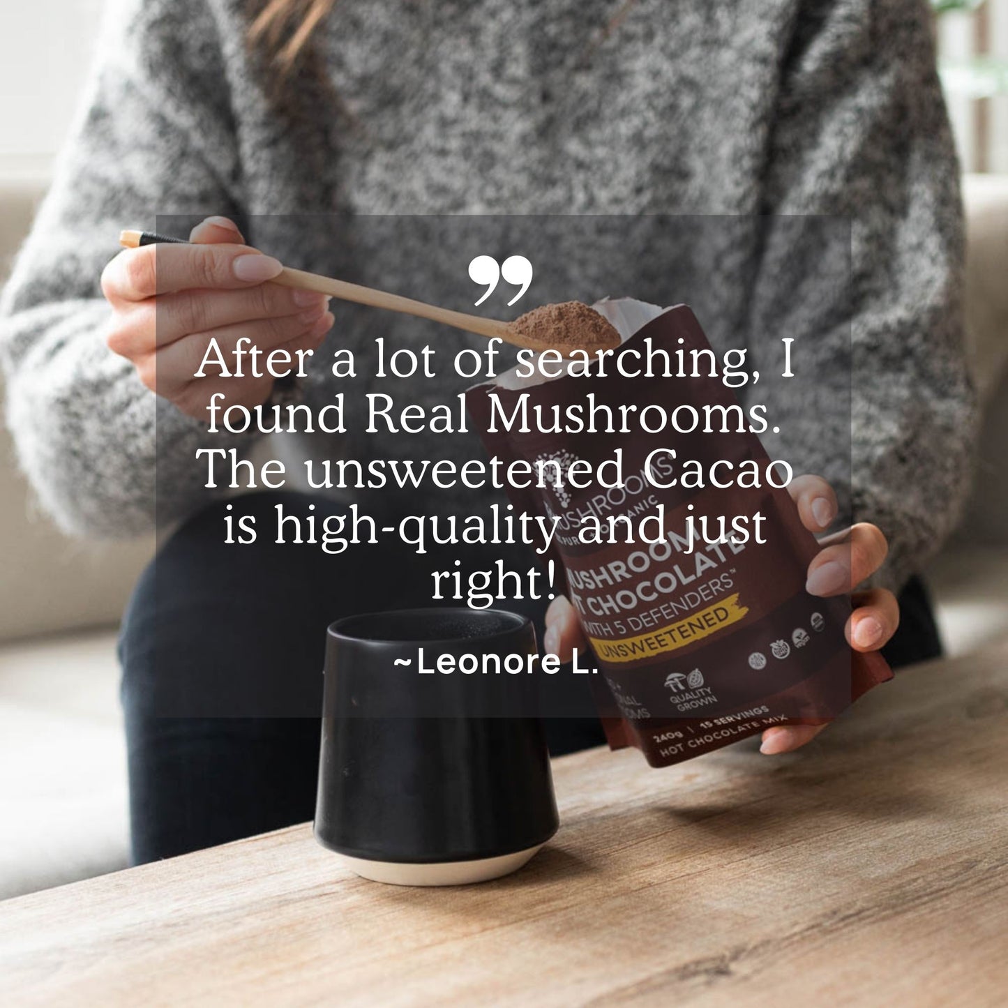 A person gently stirs their drink with a wooden spoon, holding a container labeled "Mushroom Hot Chocolate Mix" by Real Mushrooms. The text overlay features a testimonial highlighting the rich heirloom cacao and organic mushroom extract, perfect for a warming vegan treat.