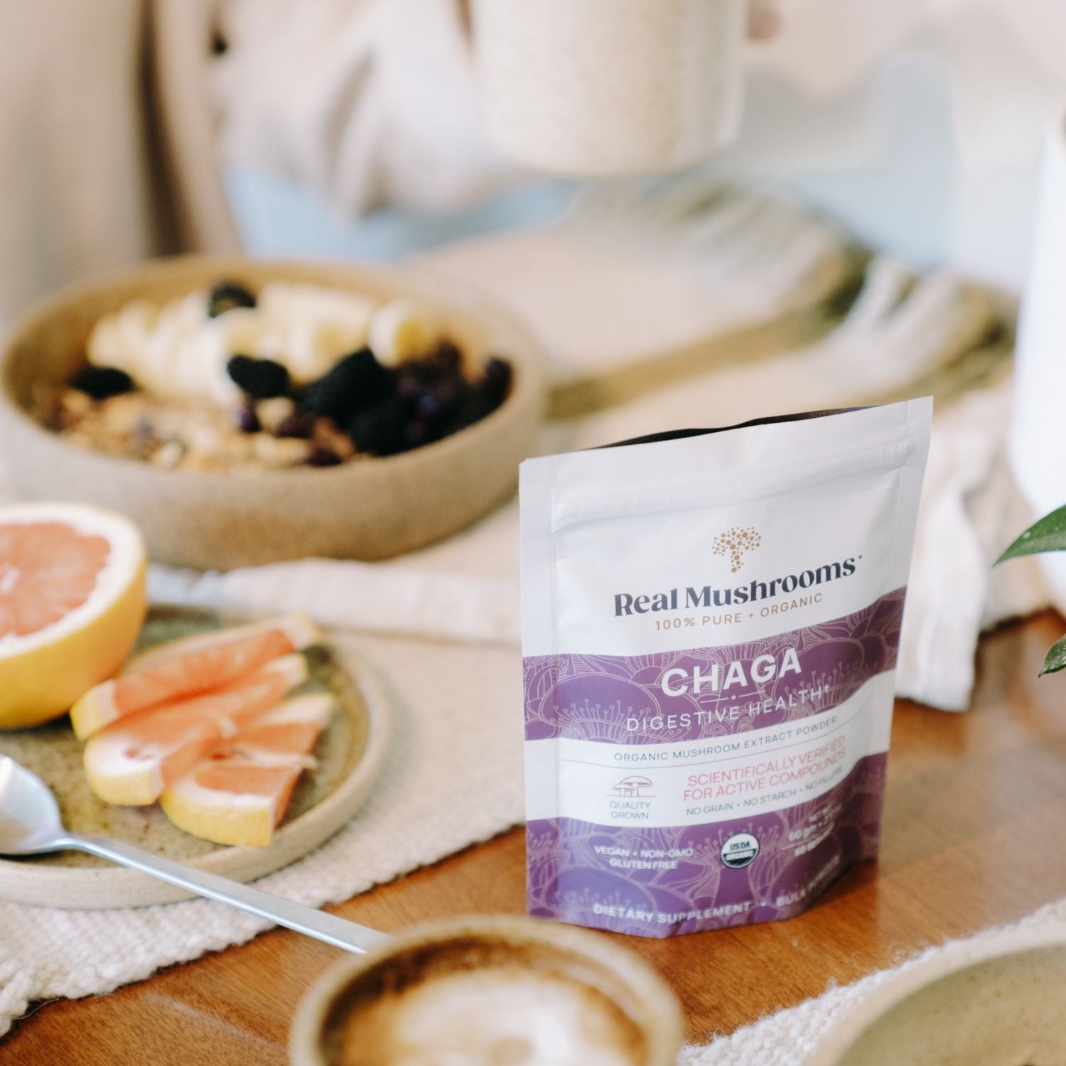 Real Mushrooms Organic Chaga Extract Powder sits beside a bowl of fruit, grapefruit slices, and coffee—an ideal daily immune support boost.