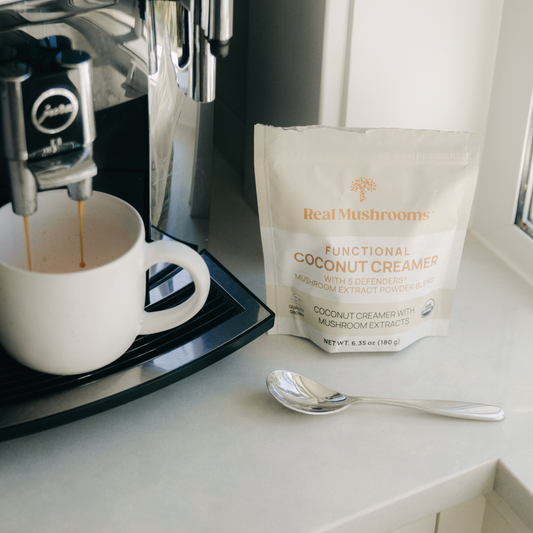 Enjoy a coffee machine set with a bag of coffee, spoon, and Real Mushrooms Functional Coconut Creamer - Powder for a delicious dairy-free experience.