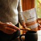 Someone scoops Real Mushrooms Organic Cordyceps Mushroom Extract Powder – Bulk Supplement into a black mug near a window.