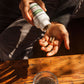 A person pours Real Mushrooms Turkey Tail Mushroom Capsules from a white bottle into their hand over a wooden table with water, highlighting their immune support benefits.