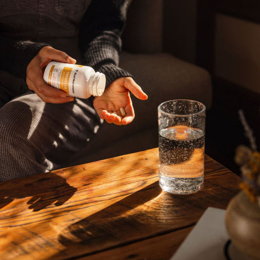 A person pours Real Mushrooms Organic Tremella Extract Capsules from a white bottle into their hand, with water nearby—highlighting skin, hair, and nail health benefits from beta-glucan-rich organic tremella.
