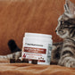 A tabby cat is lounging beside a container of Real Mushrooms' Mushroom Relax Pet Chews, marketed as a relaxation aid for pets with soothing Reishi mushroom extracts.