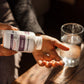 A person pours a Real Mushrooms Organic Chaga Extract Capsule, packed with beta-glucans, into their hand next to a glass of water on a wooden table.