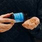 A person holds a blue Real Mushrooms bottle labeled "RealRest," pouring pills into their hand, each infused with calming Reishi, Valerian, and Lemon Balm.